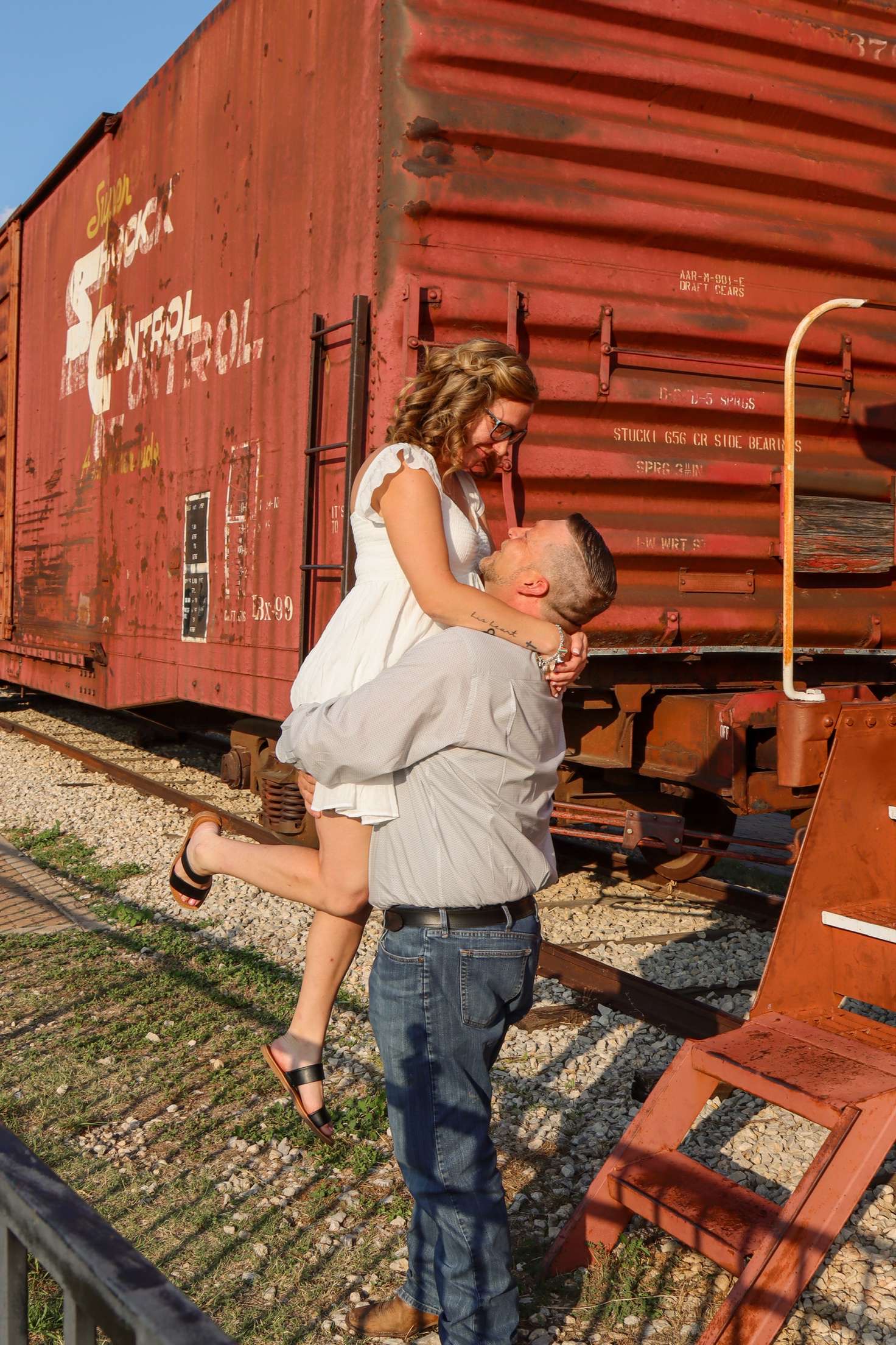 Devon lifting Lindy in front of a red train car.